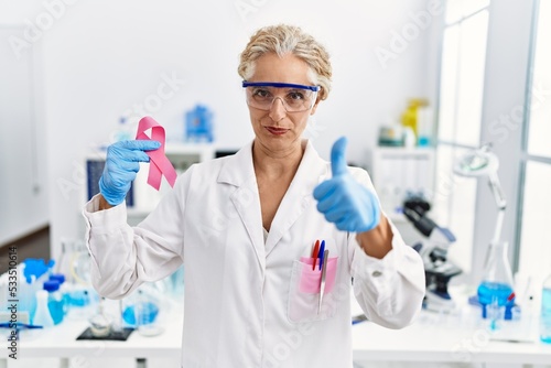 Middle age blonde woman working at laboratory looking for breast cancer cure smiling happy and positive  thumb up doing excellent and approval sign