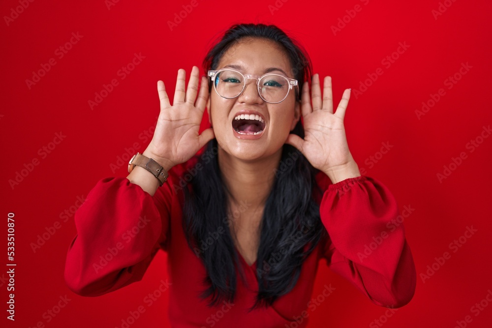 Asian young woman standing over red background smiling cheerful playing peek a boo with hands showing face. surprised and exited Asian young woman standing over red background smiling cheerful playing peek a boo with hands showing face. surprised and exited