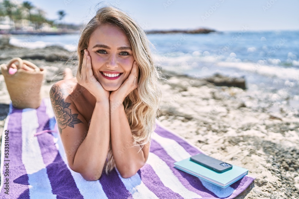 Young blonde girl wearing bikini lying on the towel at the beach.