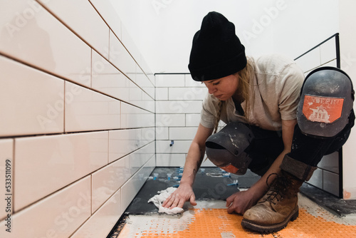 Фотография a female trades worker lays tile in a bathroom remodel