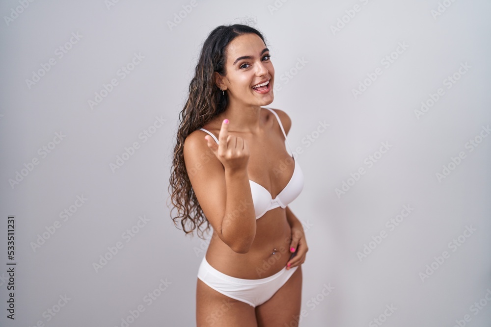 Young hispanic woman wearing white lingerie beckoning come here gesture with hand inviting welcoming happy and smiling Young hispanic woman wearing white lingerie beckoning come here gesture with hand inviting welcoming happy and smiling