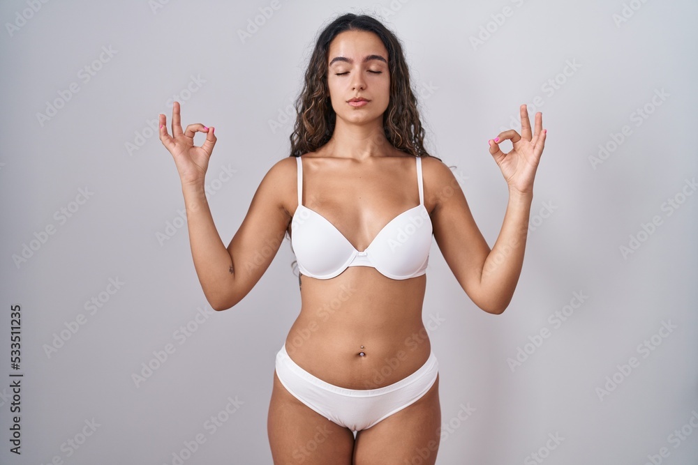 Young hispanic woman wearing white lingerie relaxed and smiling with eyes closed doing meditation gesture with fingers. yoga concept. Young hispanic woman wearing white lingerie relaxed and smiling with eyes closed doing meditation gesture with fingers. yoga concept.