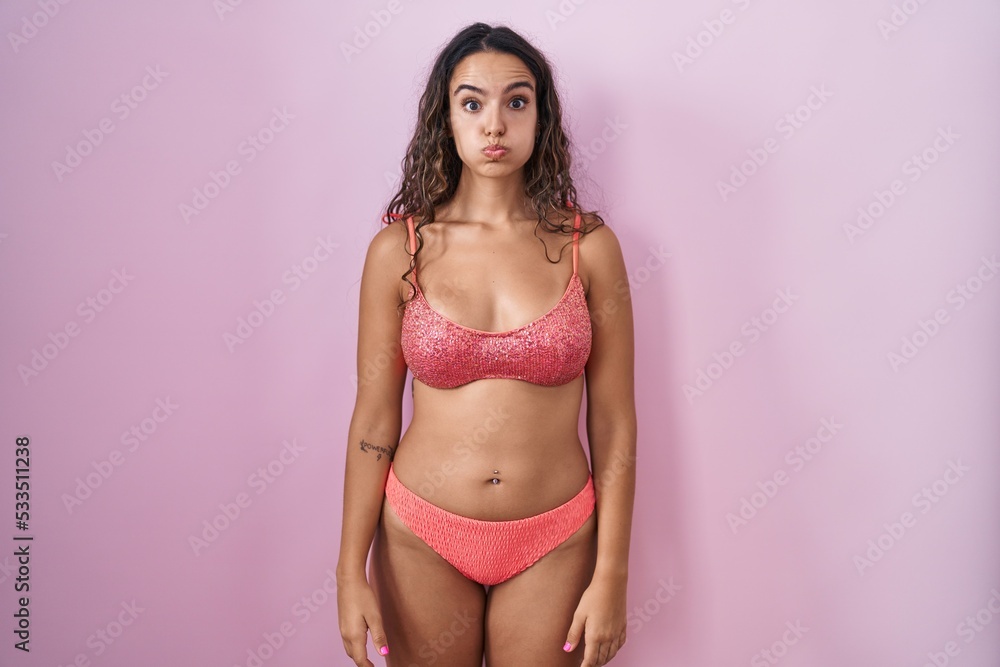 Naklejka premium Young hispanic woman wearing lingerie over pink background puffing cheeks with funny face. mouth inflated with air, crazy expression.