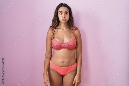 Young hispanic woman wearing lingerie over pink background puffing cheeks with funny face. mouth inflated with air, crazy expression.