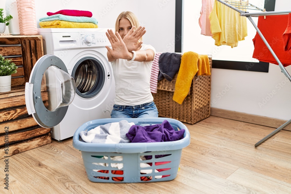 Young caucasian woman doing laundry with clothes in the basket rejection expression crossing arms and palms doing negative sign, angry face Young caucasian woman doing laundry with clothes in the basket rejection expression crossing arms and palms doing negative sign, angry face
