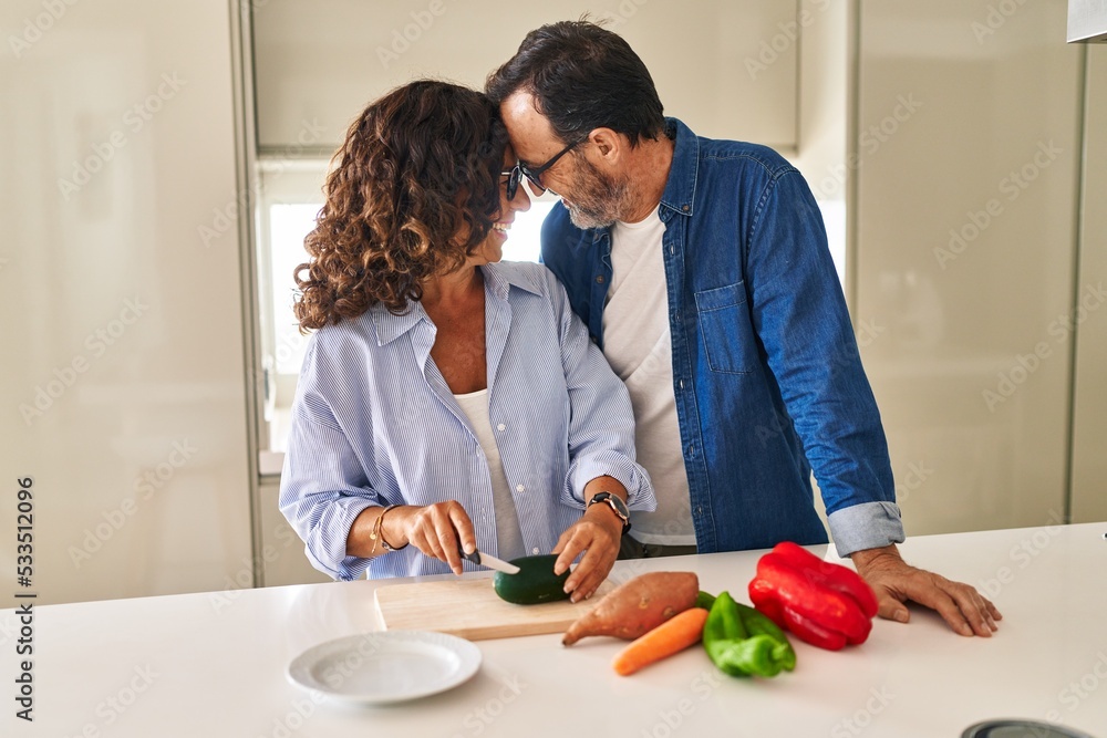 Middle age hispanic couple hugging each other cooking at kitchen Middle age hispanic couple hugging each other cooking at kitchen
