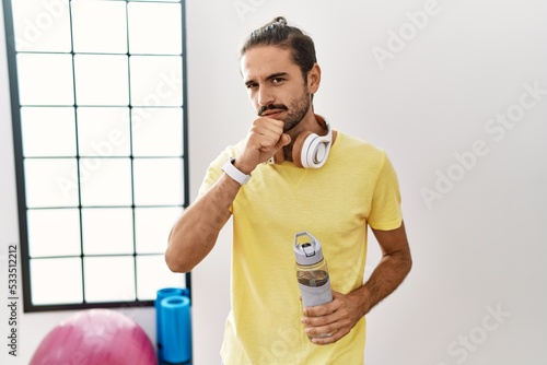 Young hispanic man wearing sportswear and drinking water at the gym feeling unwell and coughing as symptom for cold or bronchitis. health care concept.