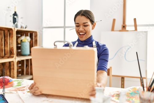 Young latin woman smiling confident opening draw briefcase at art studio