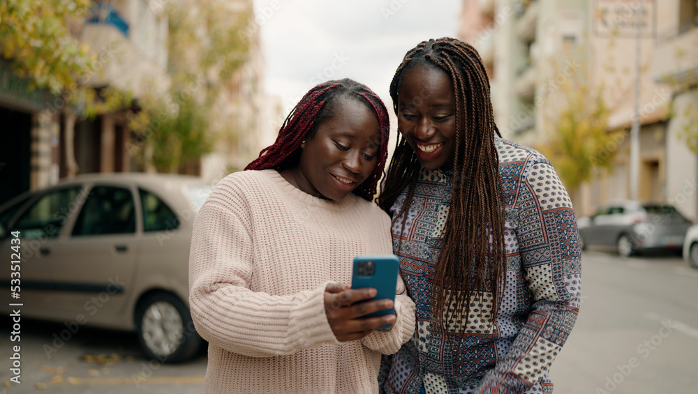 Two african american friends smiling confident using smartphone at street Two african american friends smiling confident using smartphone at street