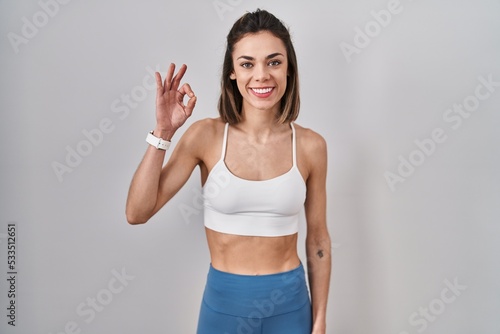 Hispanic woman wearing sportswear over isolated background smiling positive doing ok sign with hand and fingers. successful expression.