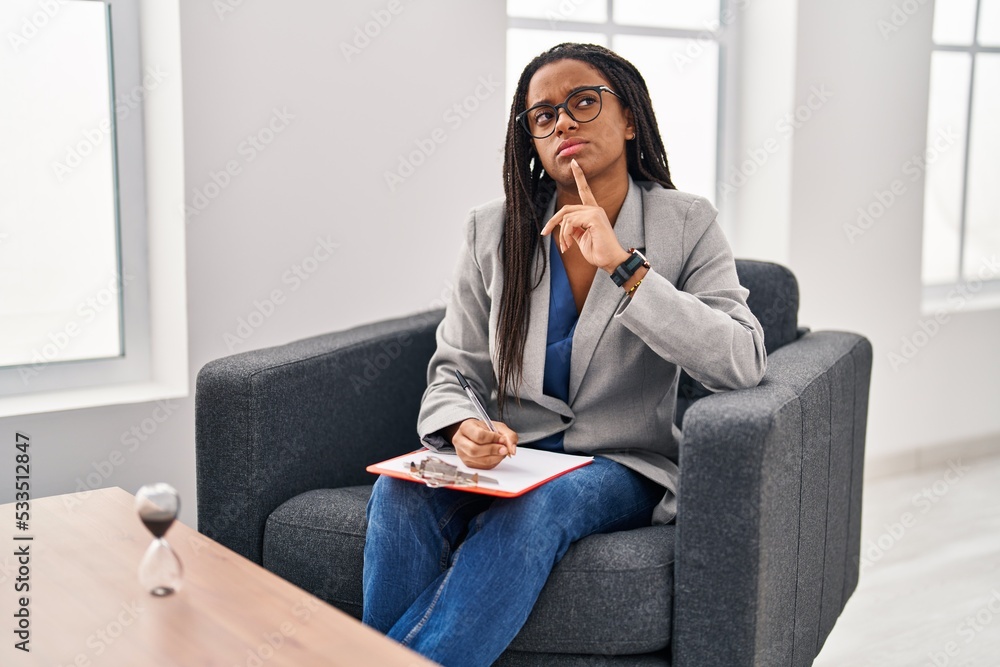 Young african american with braids working at consultation office thinking concentrated about doubt with finger on chin and looking up wondering Young african american with braids working at consultation office thinking concentrated about doubt with finger on chin and looking up wondering