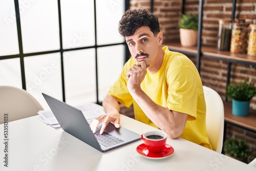 Young caucasian man using laptop drinking coffee at home
