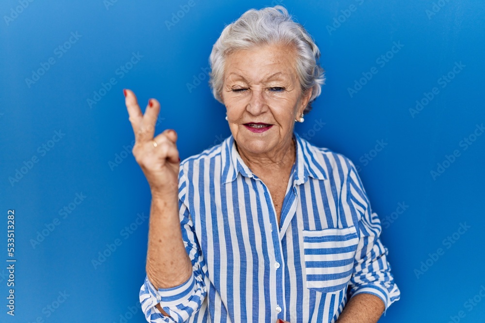 Senior woman with grey hair standing over blue background showing and pointing up with fingers number two while smiling confident and happy. Senior woman with grey hair standing over blue background showing and pointing up with fingers number two while smiling confident and happy.