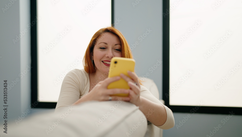 Young redhead woman using smartphone sitting on sofa at home Young redhead woman using smartphone sitting on sofa at home