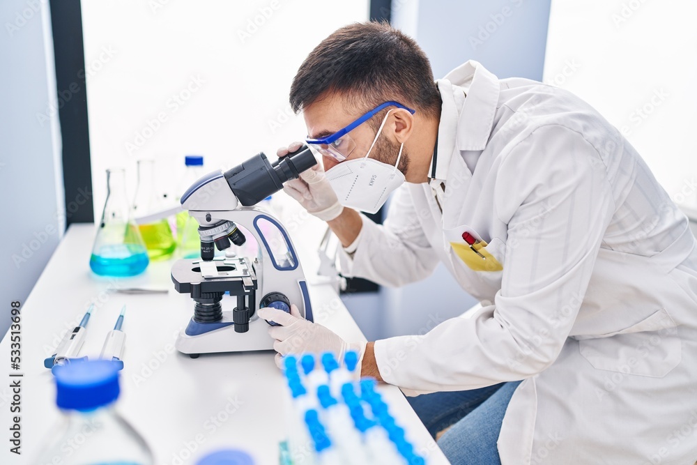 Young hispanic man scientist using microscope wearing medical mask at laboratory Young hispanic man scientist using microscope wearing medical mask at laboratory