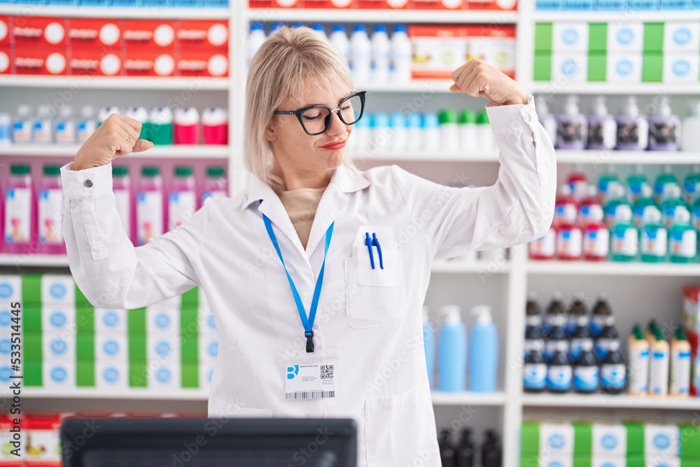 Young caucasian woman working at pharmacy drugstore showing arms muscles smiling proud. fitness concept.