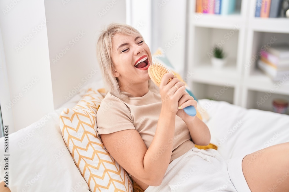 Young blonde woman singing song using brush as a microphone at bedroom Young blonde woman singing song using brush as a microphone at bedroom