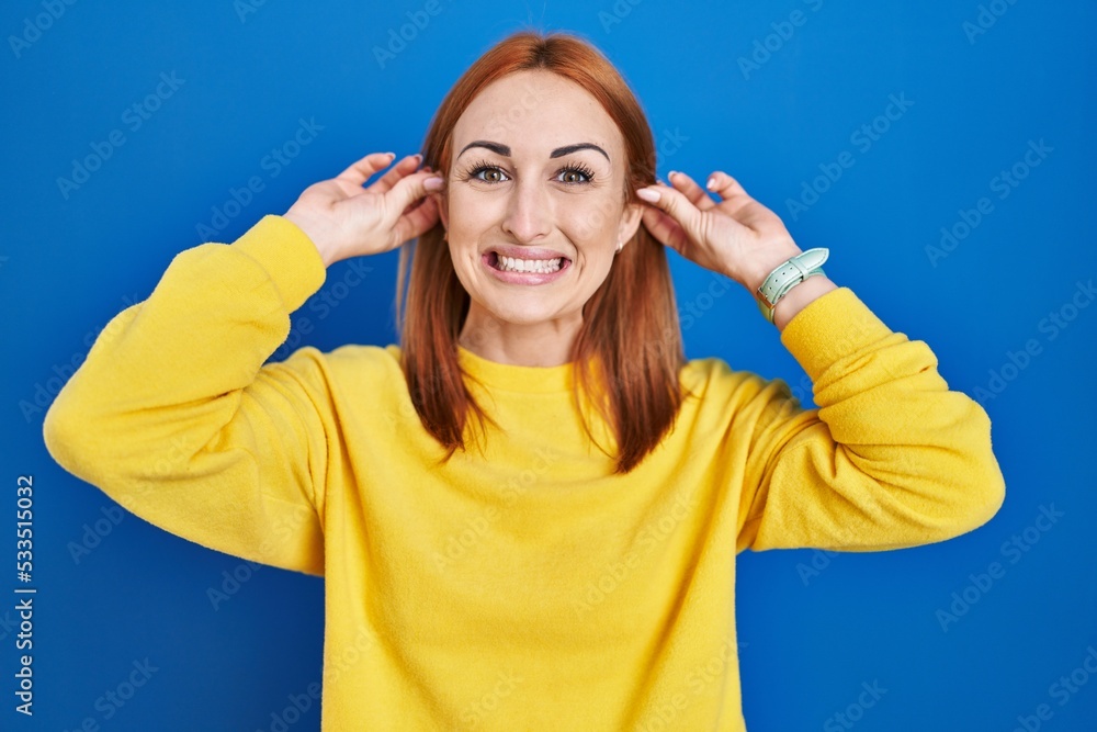 Young woman standing over blue background smiling pulling ears with fingers, funny gesture. audition problem Young woman standing over blue background smiling pulling ears with fingers, funny gesture. audition problem