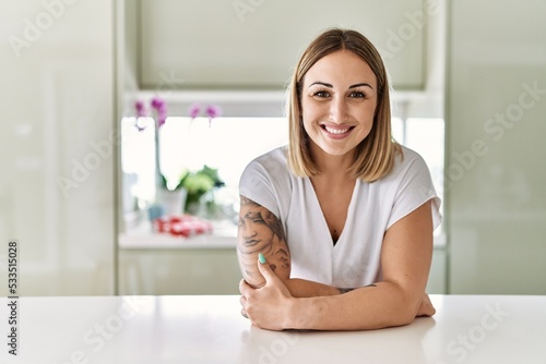 Young caucasian girl smiling happy leaning on the table standing at the kitchen.