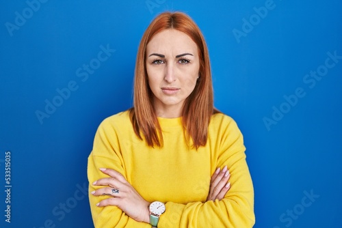 Young woman standing over blue background skeptic and nervous, disapproving expression on face with crossed arms. negative person.