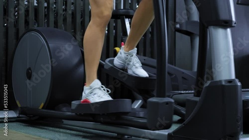 Woman legs using elliptic trainer in gym. Female using exercise machines in fitness center. Healthy lifestyle. Close-up in 4K, UHD
