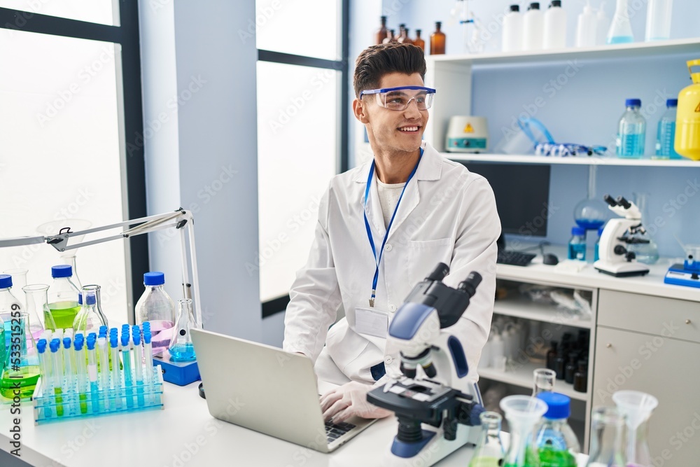 Young hispanic man wearing scientist uniform using laptop at laboratory Young hispanic man wearing scientist uniform using laptop at laboratory