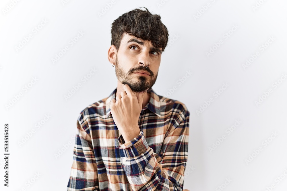 Obraz premium Hispanic man with beard standing over isolated background with hand on chin thinking about question, pensive expression. smiling with thoughtful face. doubt concept.