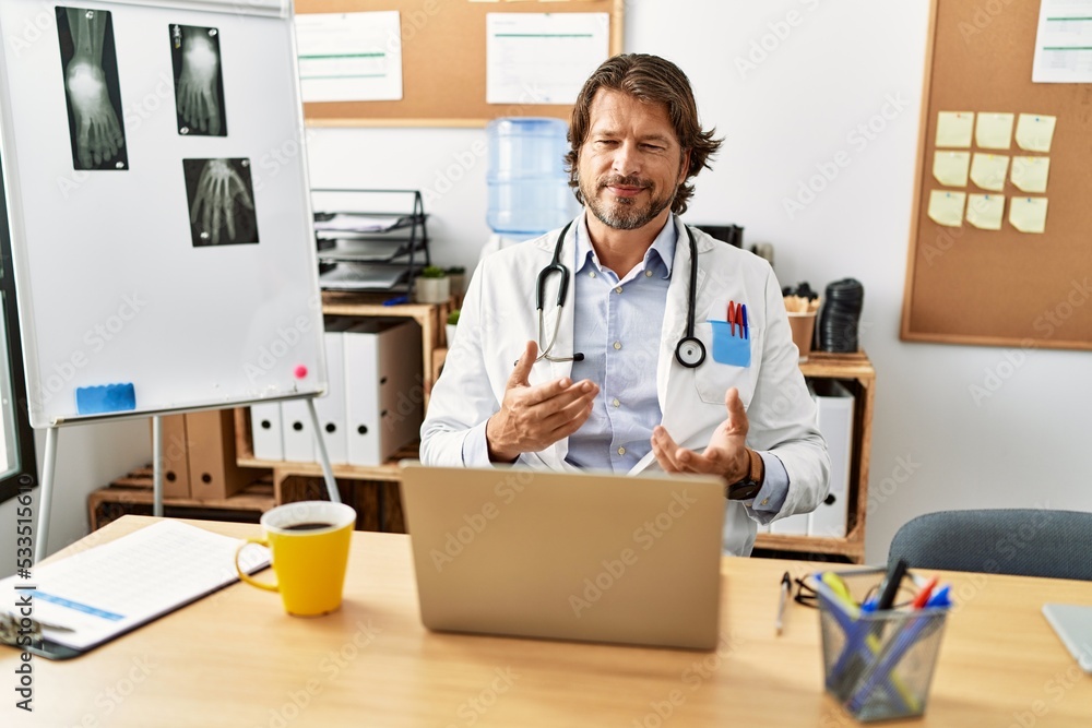Middle age caucasian man wearing doctor uniform having video call al clinic Middle age caucasian man wearing doctor uniform having video call al clinic
