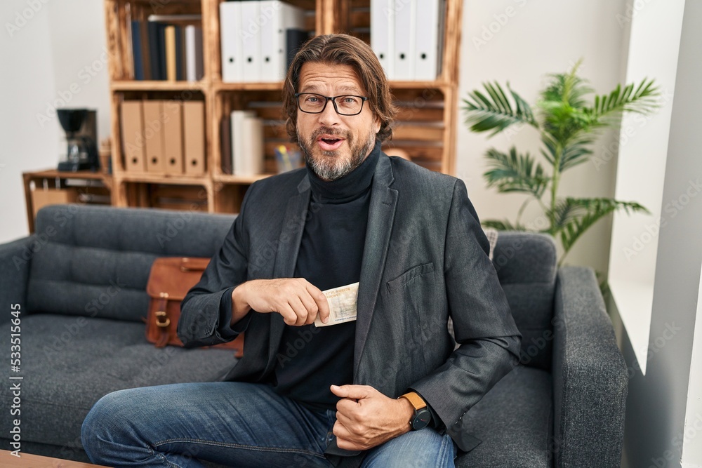Handsome middle age man at consultation office keeping money smiling and laughing hard out loud because funny crazy joke. Handsome middle age man at consultation office keeping money smiling and laughing hard out loud because funny crazy joke.