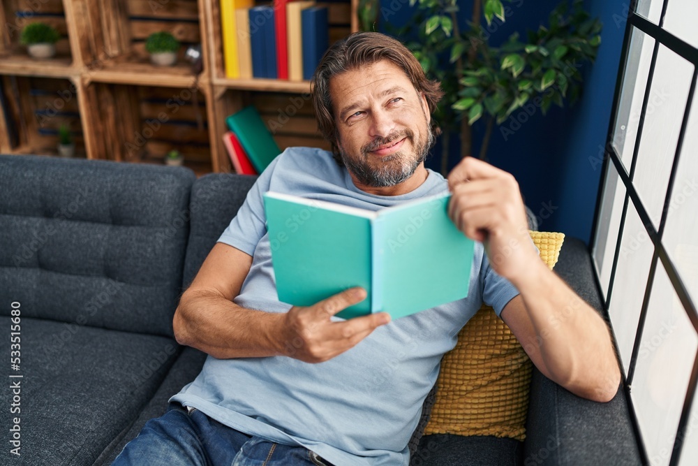 Middle age man reading book sitting on sofa at home Middle age man reading book sitting on sofa at home