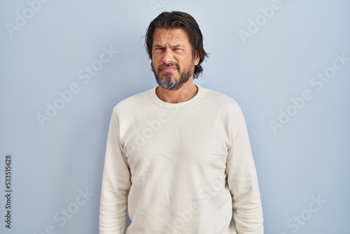 Handsome middle age man wearing casual sweater over blue background skeptic and nervous, frowning upset because of problem. negative person. photo