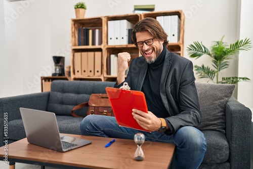 Handsome middle age man working at consultation office very happy and excited doing winner gesture with arms raised, smiling and screaming for success. celebration concept.