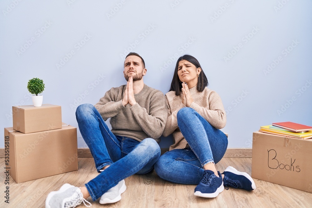 Young couple moving to a new home begging and praying with hands together with hope expression on face very emotional and worried. begging. Young couple moving to a new home begging and praying with hands together with hope expression on face very emotional and worried. begging.