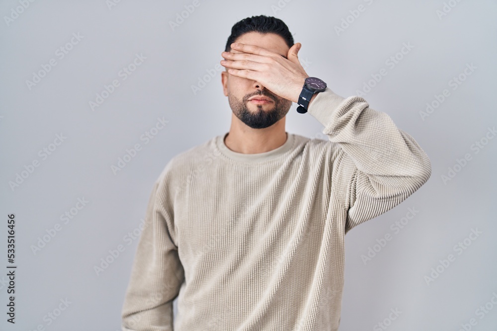 Young handsome man standing over isolated background covering eyes with hand, looking serious and sad. sightless, hiding and rejection concept Young handsome man standing over isolated background covering eyes with hand, looking serious and sad. sightless, hiding and rejection concept