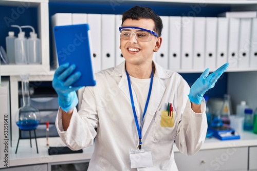 Non binary person working at scientist laboratory using tablet celebrating achievement with happy smile and winner expression with raised hand
