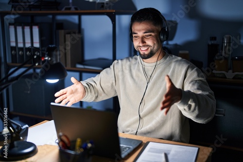 Young handsome man working using computer laptop at night looking at the camera smiling with open arms for hug. cheerful expression embracing happiness.