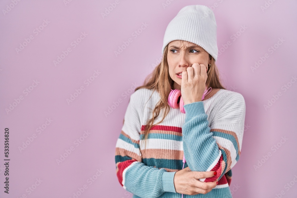 Young blonde woman standing over pink background looking stressed and nervous with hands on mouth biting nails. anxiety problem.