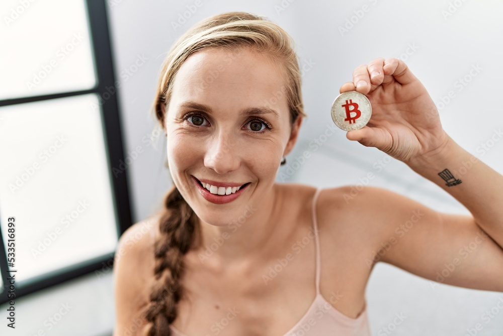 Young caucasian woman holding bitcoin sitting on sofa at home Young caucasian woman holding bitcoin sitting on sofa at home