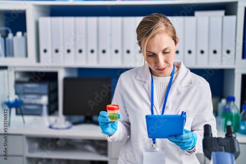 Photos Young blonde woman scientist using touchpad holding urine test tube at laborator