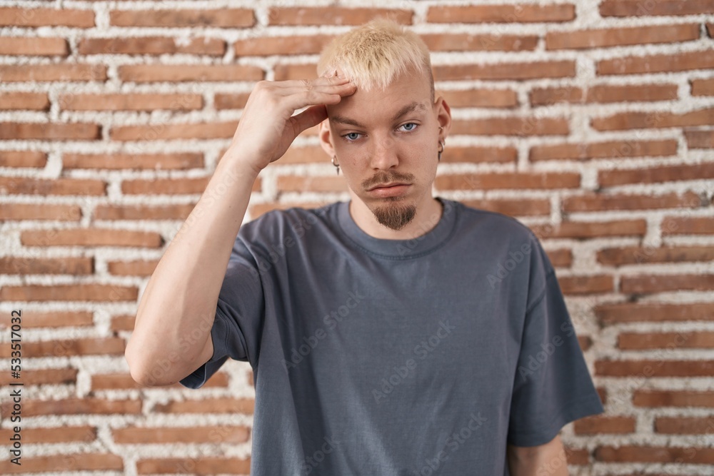 Young caucasian man standing over bricks wall worried and stressed about a problem with hand on forehead, nervous and anxious for crisis Young caucasian man standing over bricks wall worried and stressed about a problem with hand on forehead, nervous and anxious for crisis