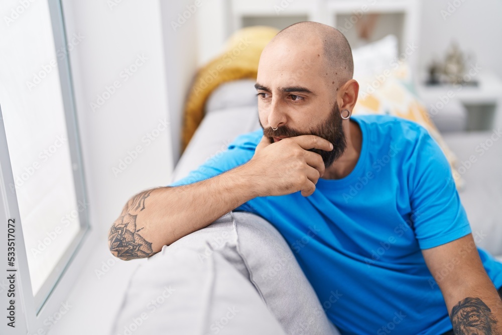 Fototapeta premium Young bald man sitting on sofa with serious expression at home