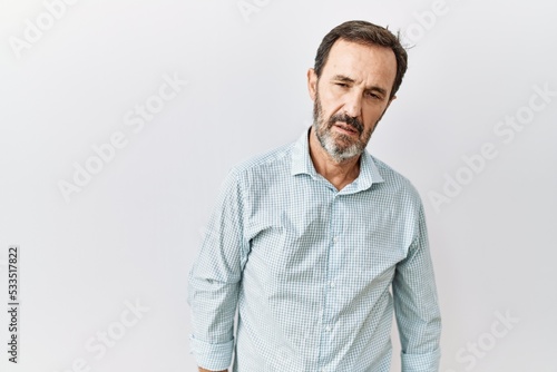 Middle age hispanic man with beard standing over isolated background looking sleepy and tired, exhausted for fatigue and hangover, lazy eyes in the morning.