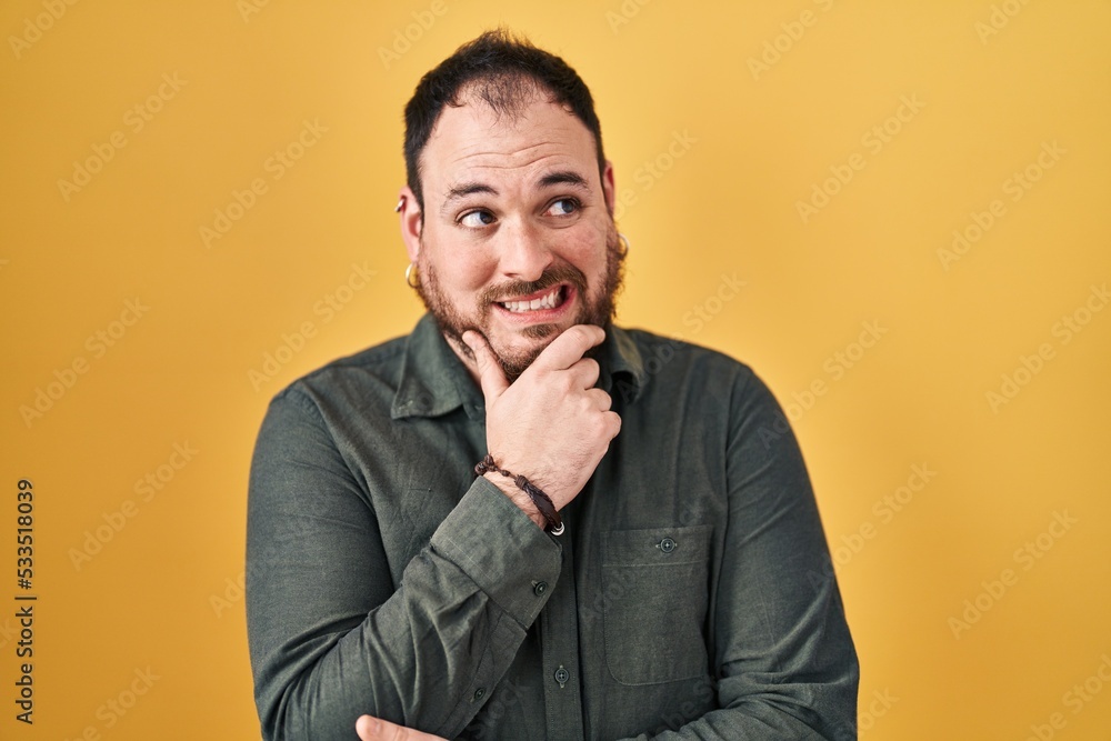 Plus size hispanic man with beard standing over yellow background thinking worried about a question, concerned and nervous with hand on chin Plus size hispanic man with beard standing over yellow background thinking worried about a question, concerned and nervous with hand on chin