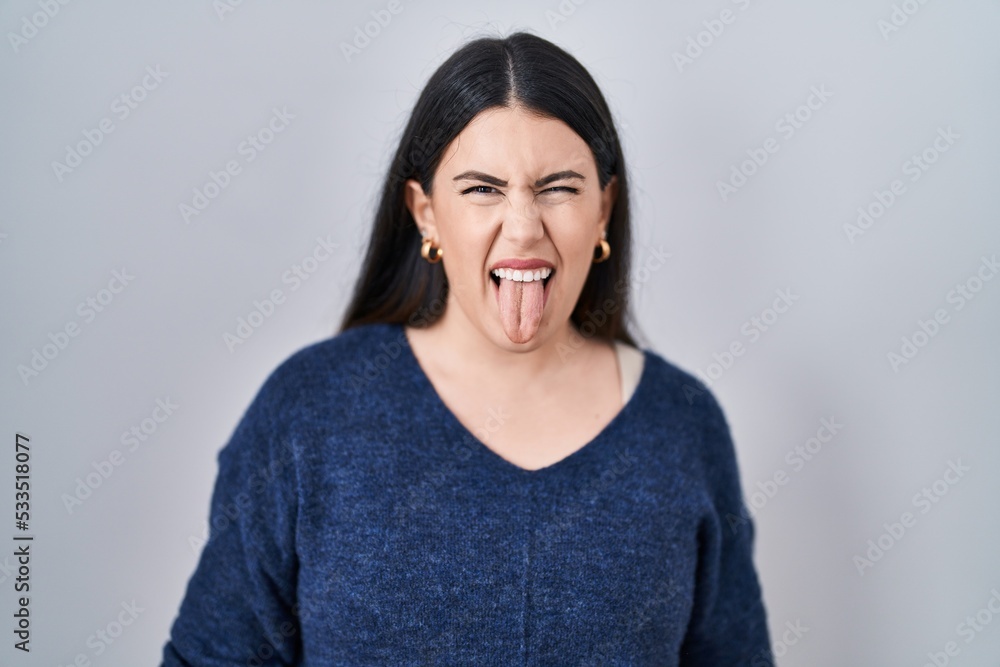 Young brunette woman standing over isolated background sticking tongue out happy with funny expression. emotion concept. Young brunette woman standing over isolated background sticking tongue out happy with funny expression. emotion concept.