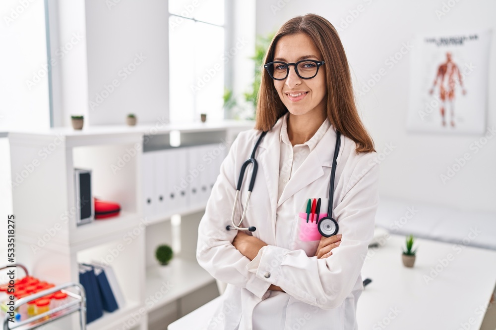 Young woman wearing medical uniform standing with arms crossed gesture at clinic