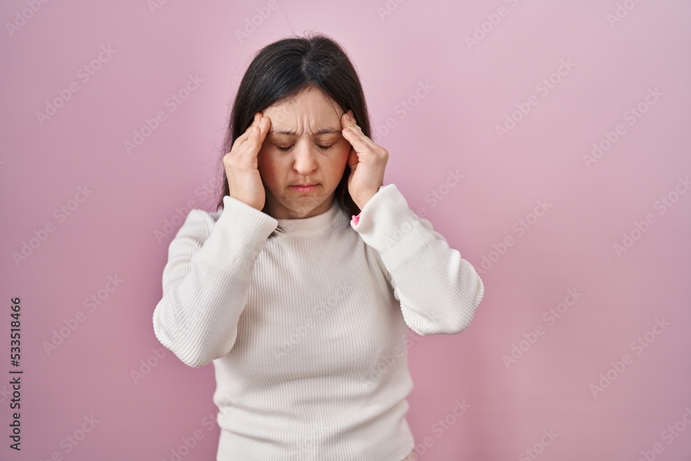 Woman with down syndrome standing over pink background with hand on head, headache because stress. suffering migraine. Woman with down syndrome standing over pink background with hand on head, headache because stress. suffering migraine.