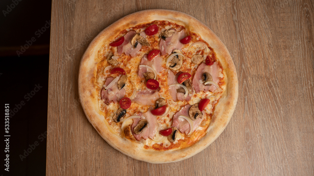 Italian pizza with cheese, ham, cherry tomatoes, onions and mushrooms on the table background Italian pizza with cheese, ham, cherry tomatoes, onions and mushrooms on the table background