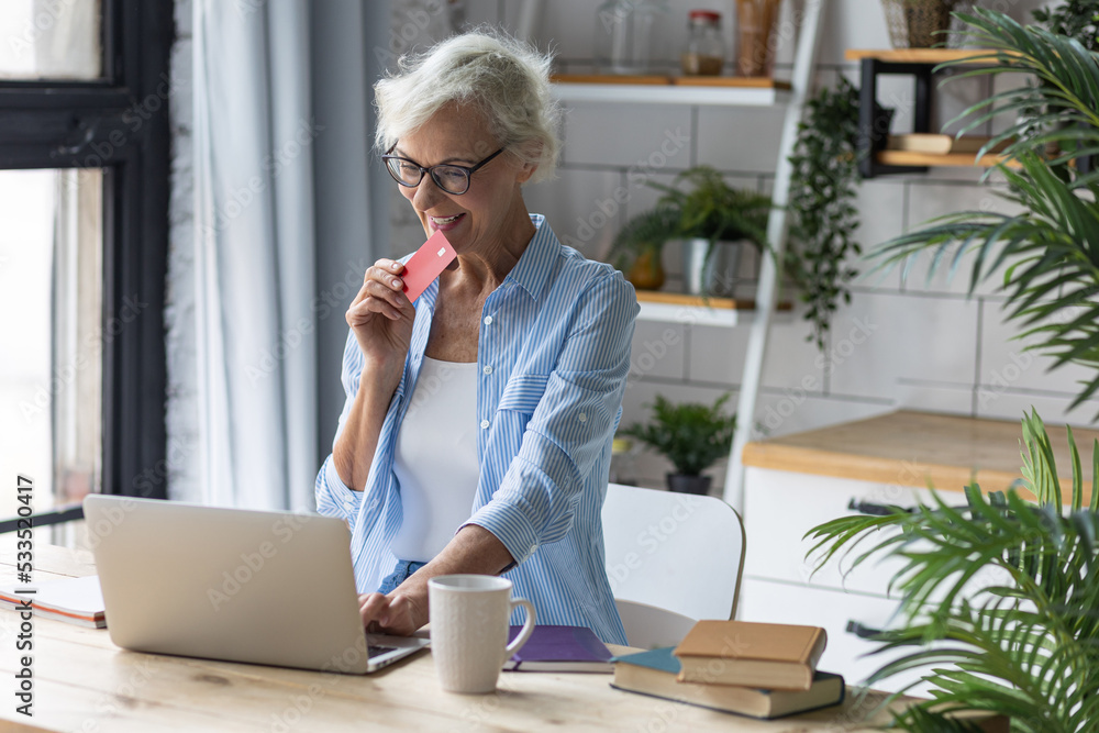 Beautiful senior woman with short grey hair and lovely smile shopping in the internet at home with a credit card. Concept of mature woman using technology Beautiful senior woman with short grey hair and lovely smile shopping in the internet at home with a credit card. Concept of mature woman using technology