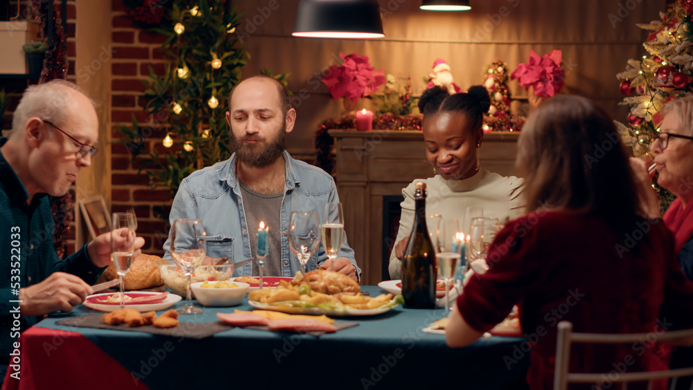 Cheerful multicultural people enjoying Christmas dinner while eating roasted chicken. Happy diverse family members enjoying traditional home cooked food wihle celebrating winter holiday together.