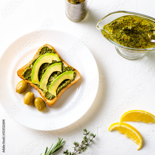 toast with avocado, olives and chimichurri sauce on a white plate. Healthy vegetarian food. White background.